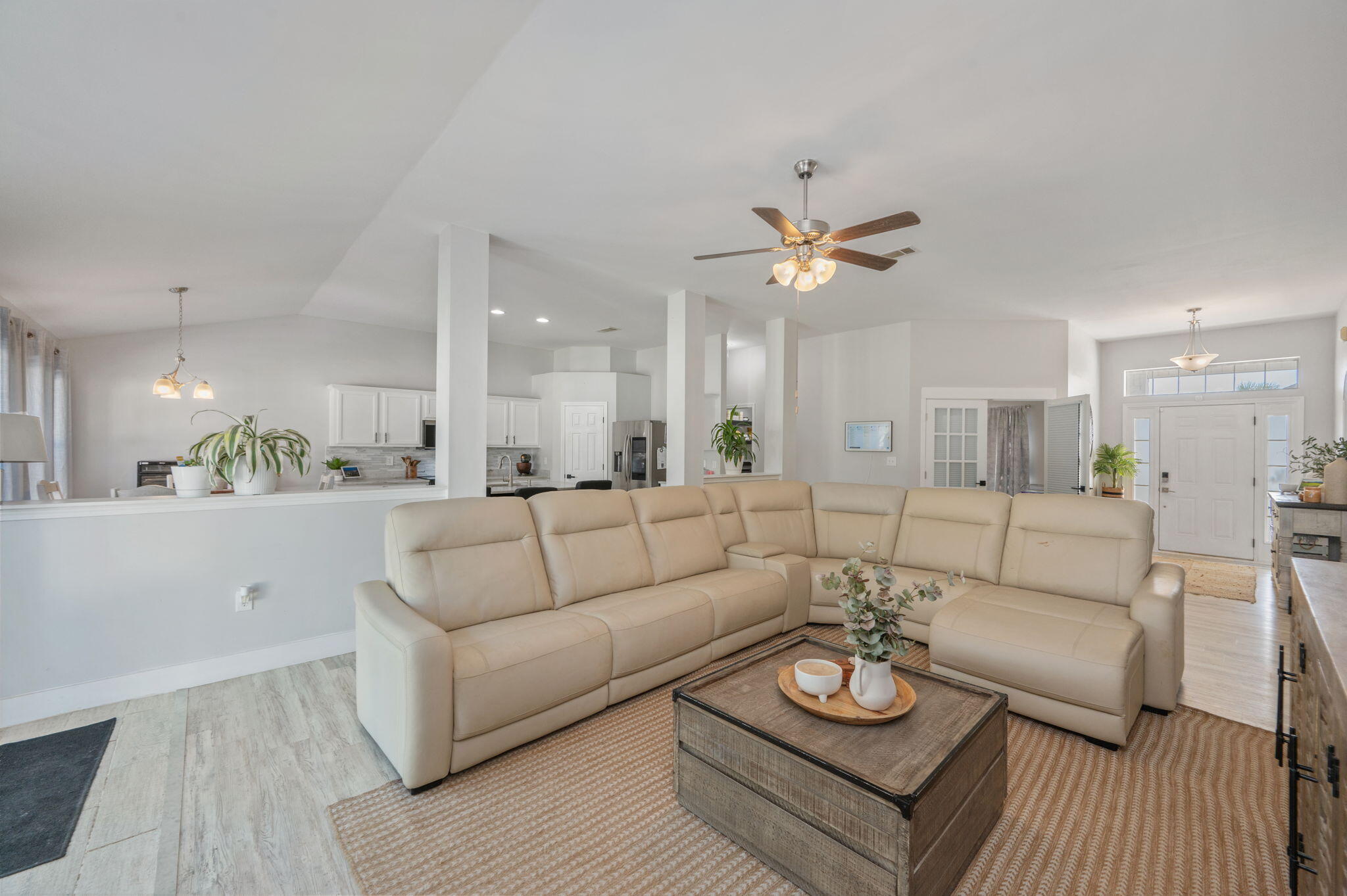 Open-plan living room with a beige sectional, wood coffee table, and adjoining white kitchen.