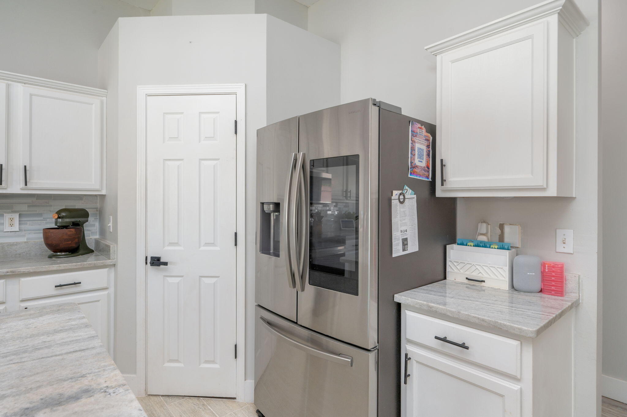 Kitchen with white cabinets, pale stone counters, and a stainless steel French-door refrigerator.