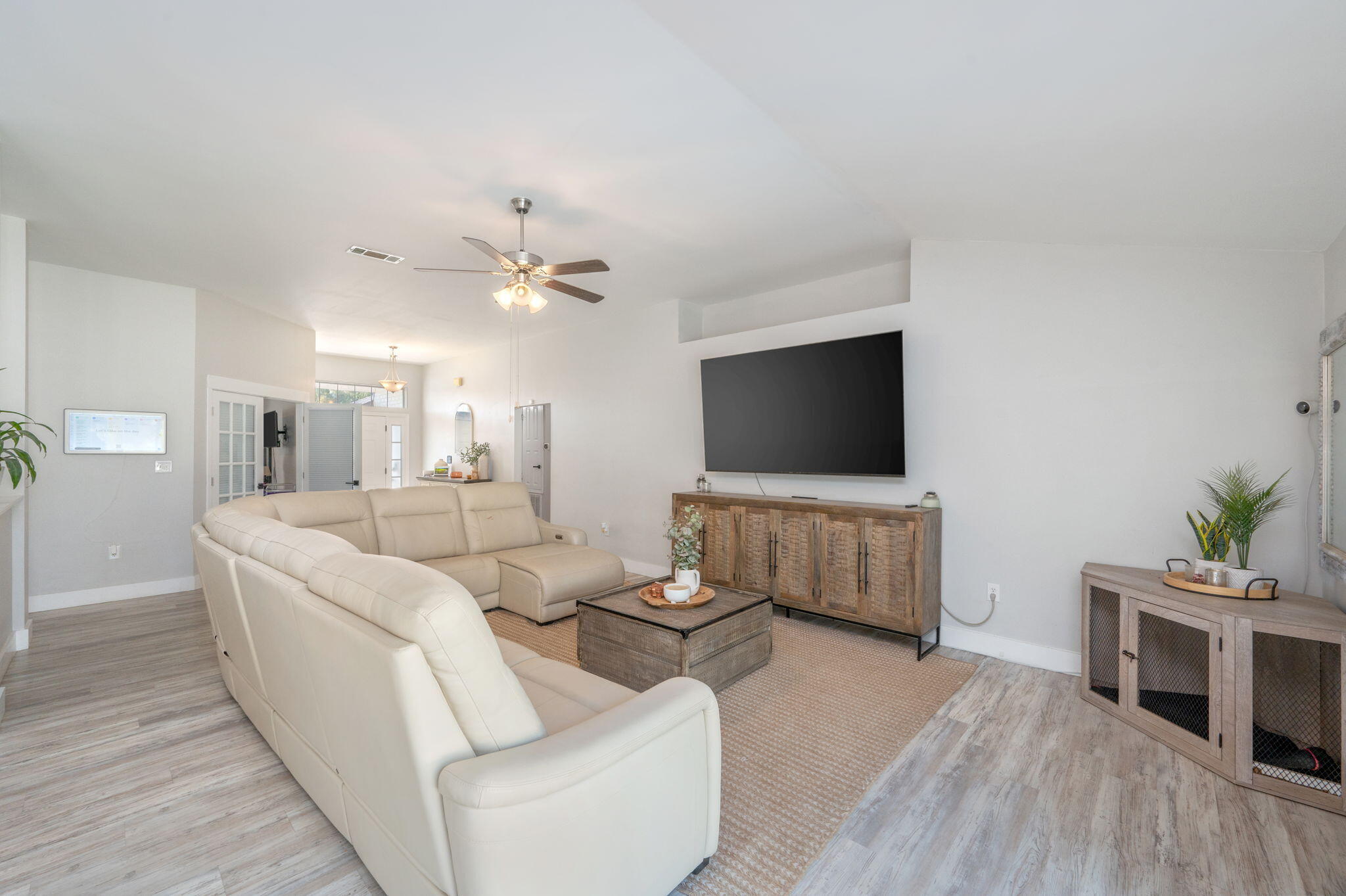 Furnished living room with a cream sectional, woven rug, and large wall-mounted television.