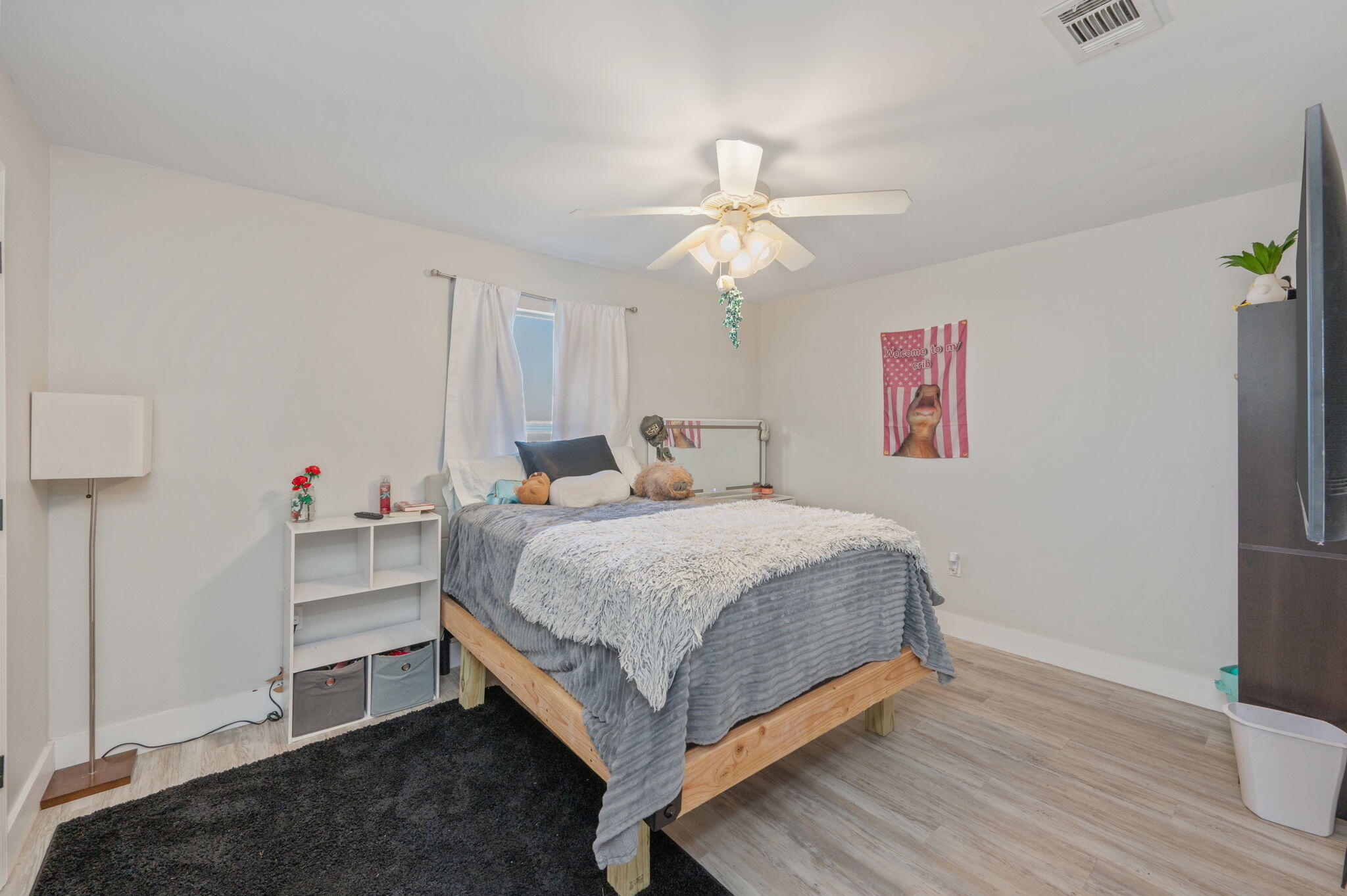 Furnished bedroom with a wooden bed, gray and white bedding, dark rug, and illuminated ceiling fan.