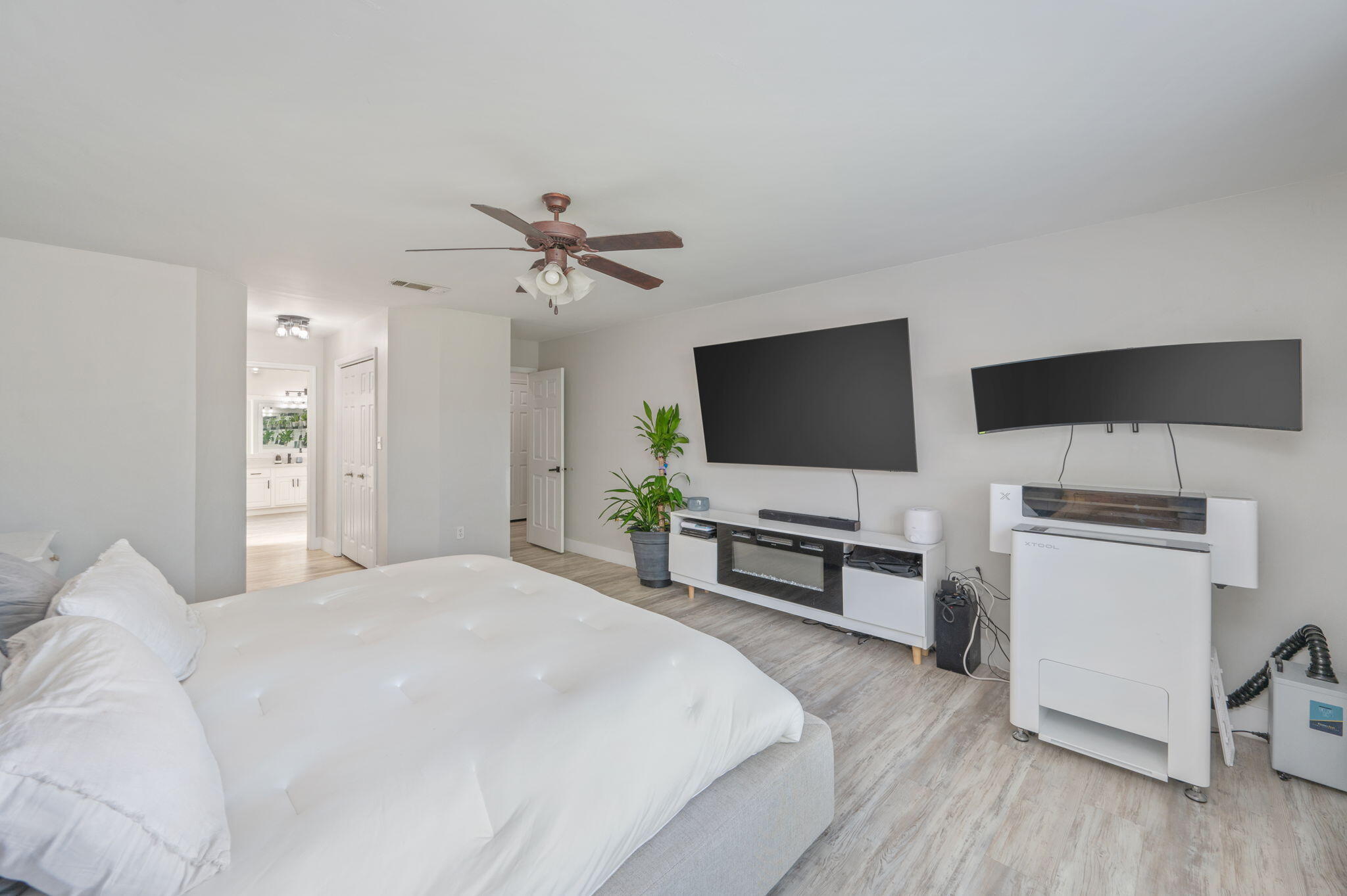 Furnished bedroom with a large white bed, two wall-mounted screens, and a doorway to the bathroom.