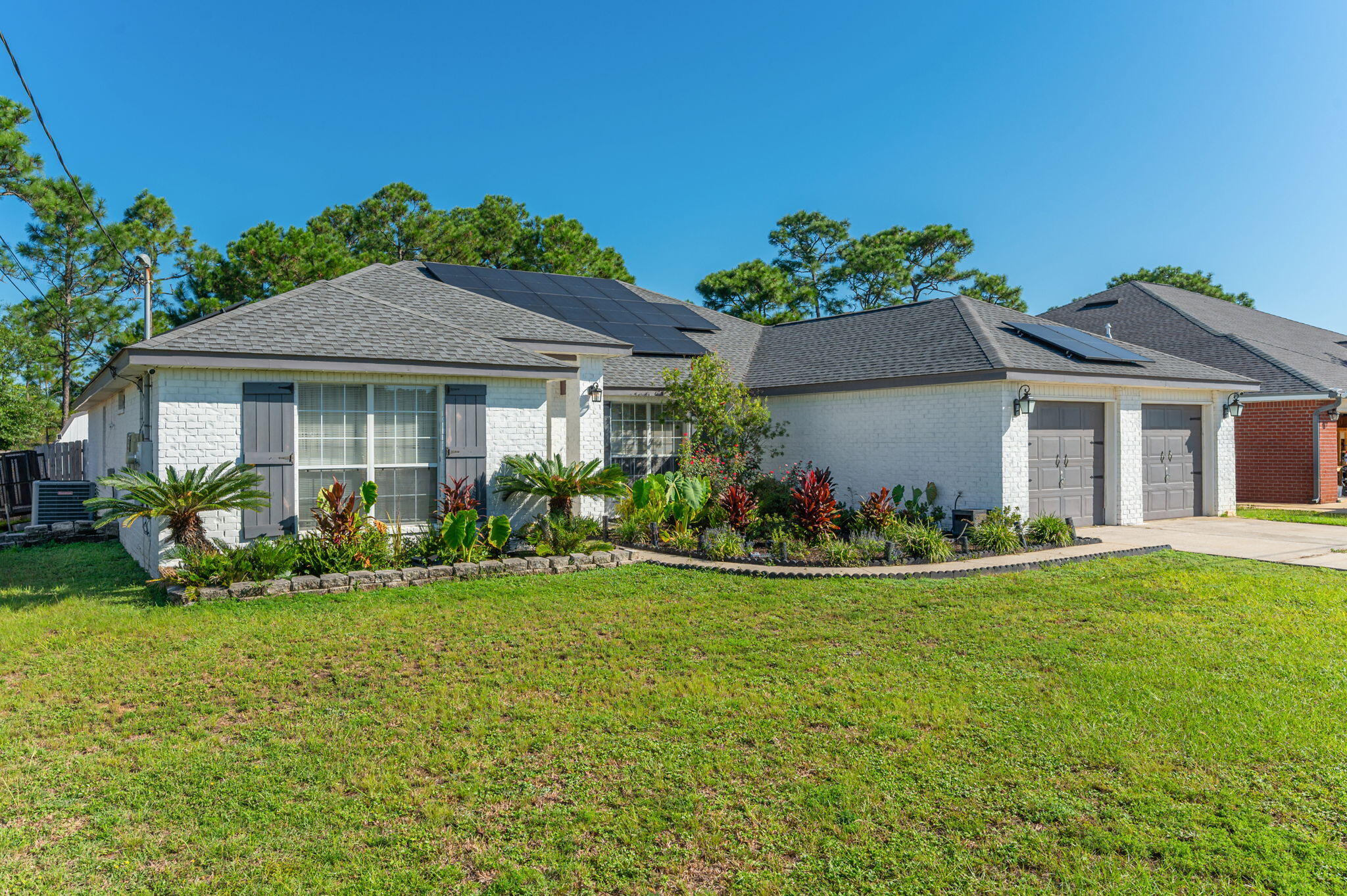 Single-story brick home with rooftop solar panels, a two-car garage, and landscaped front garden.