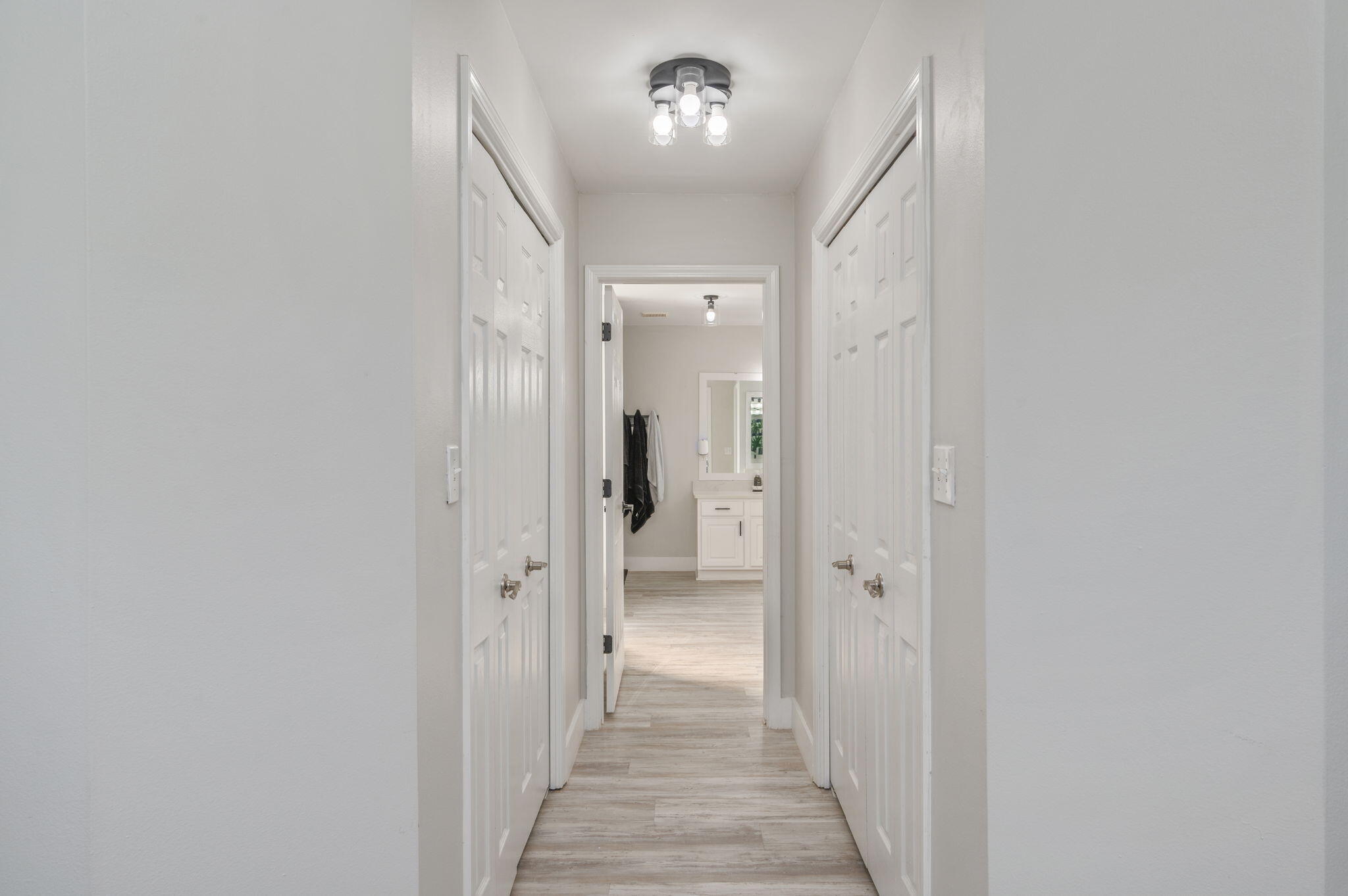 Hallway with white paneled doors and light wood-look flooring, opening to a bathroom vanity.