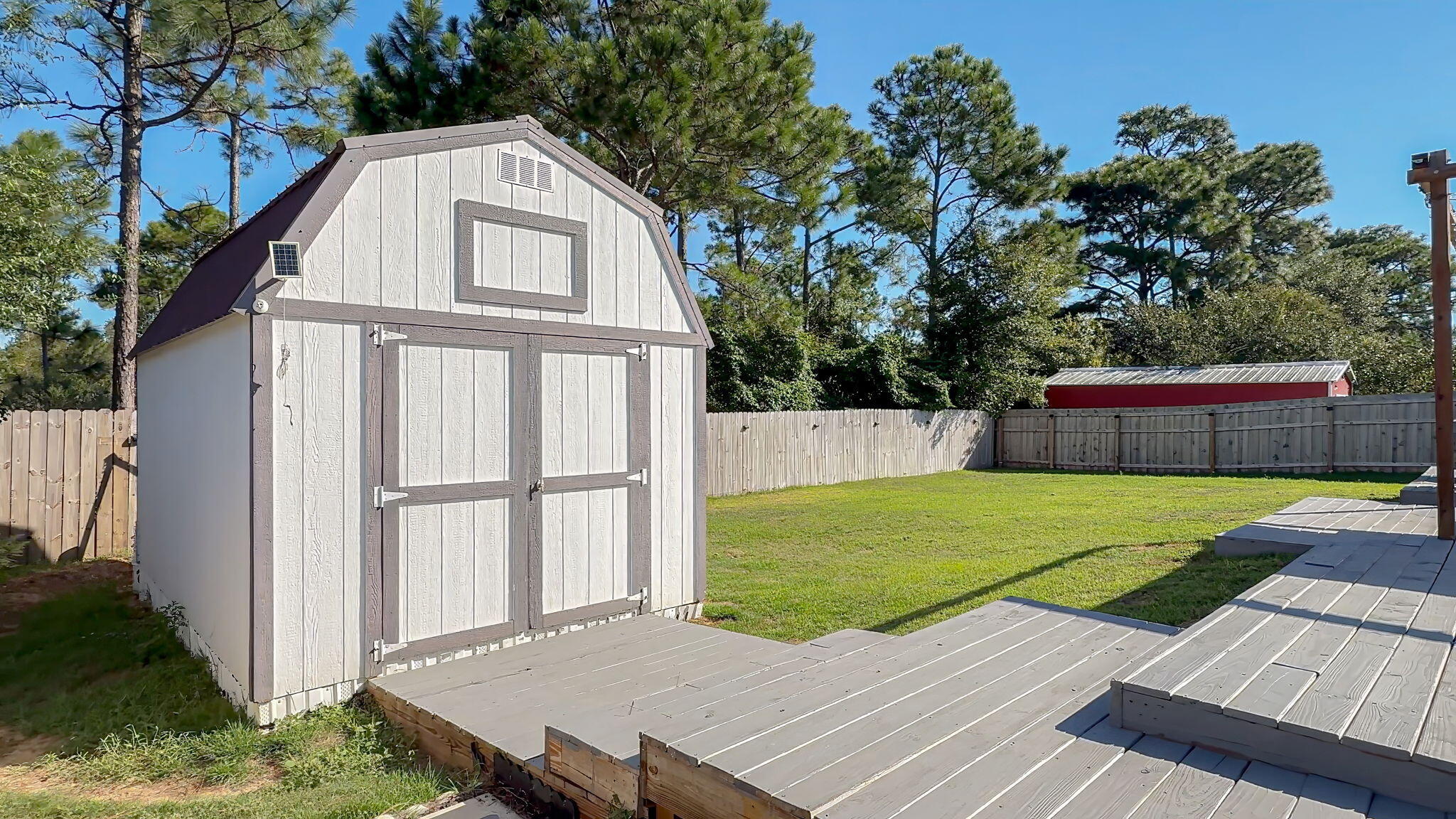 Fenced backyard with a white storage shed, raised deck, and lawn.