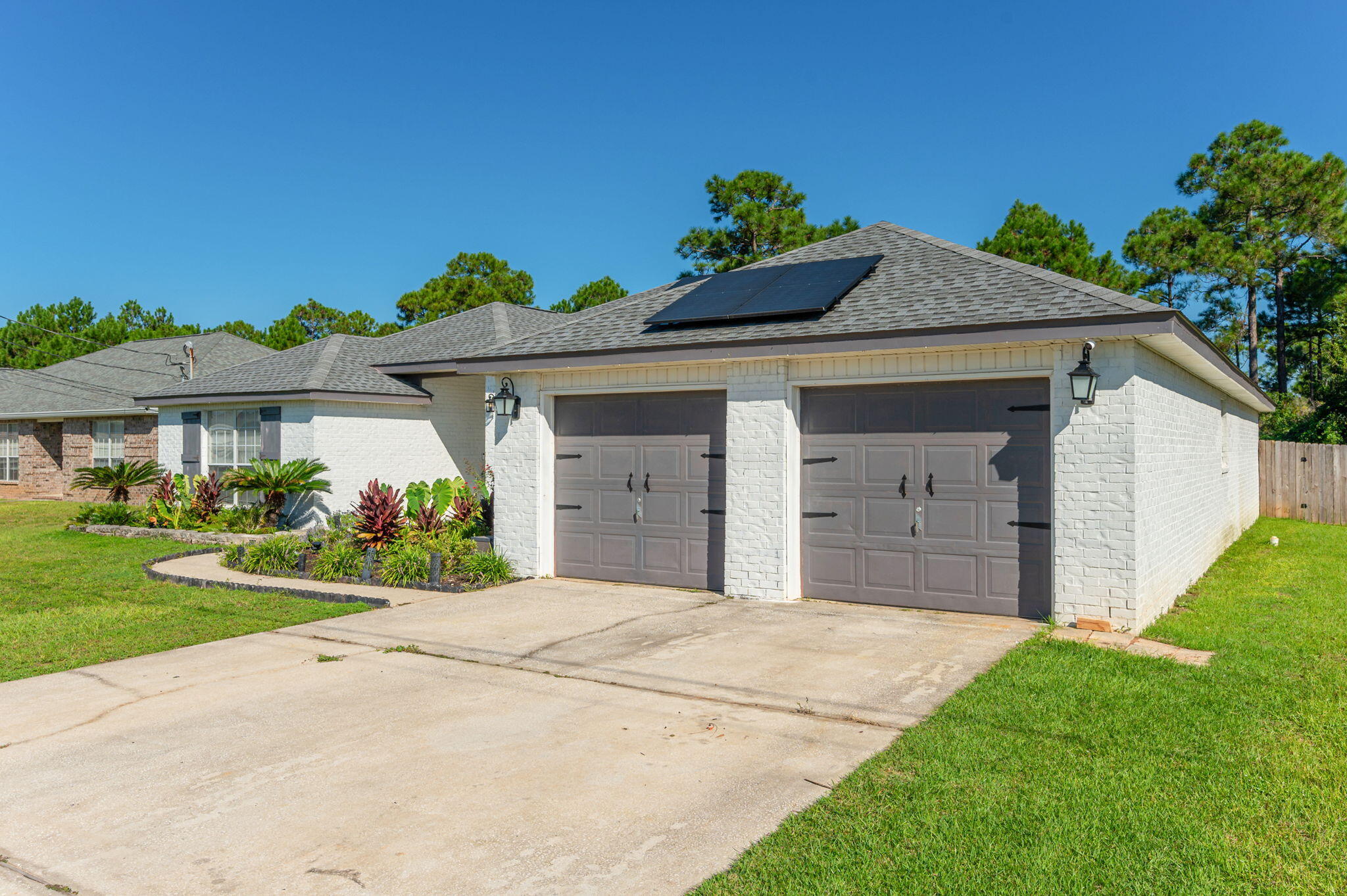 White brick home with solar panels, a two-car garage, and landscaped front yard.