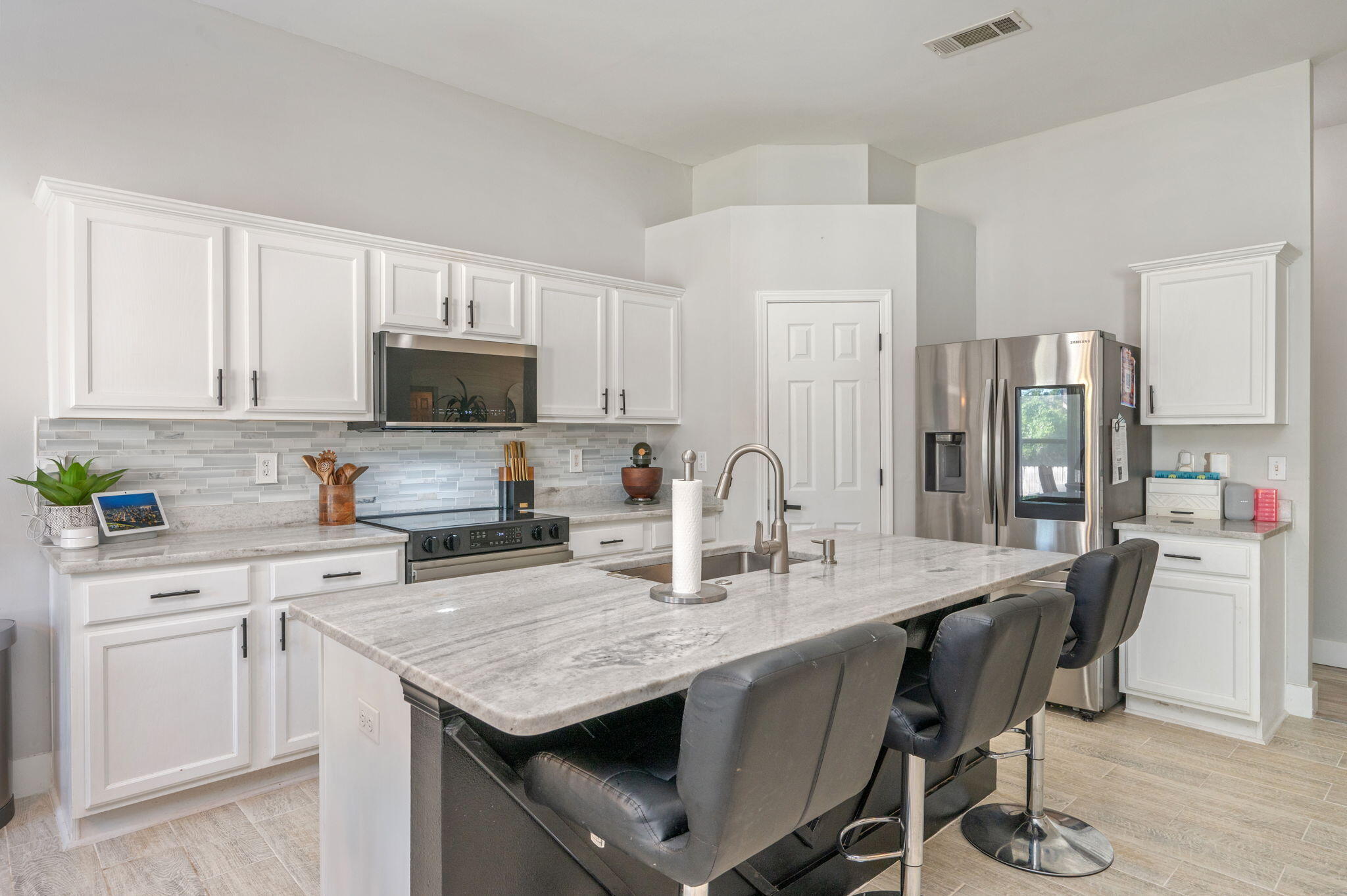 Kitchen with white cabinets, stainless appliances, and a large stone island with three bar stools.