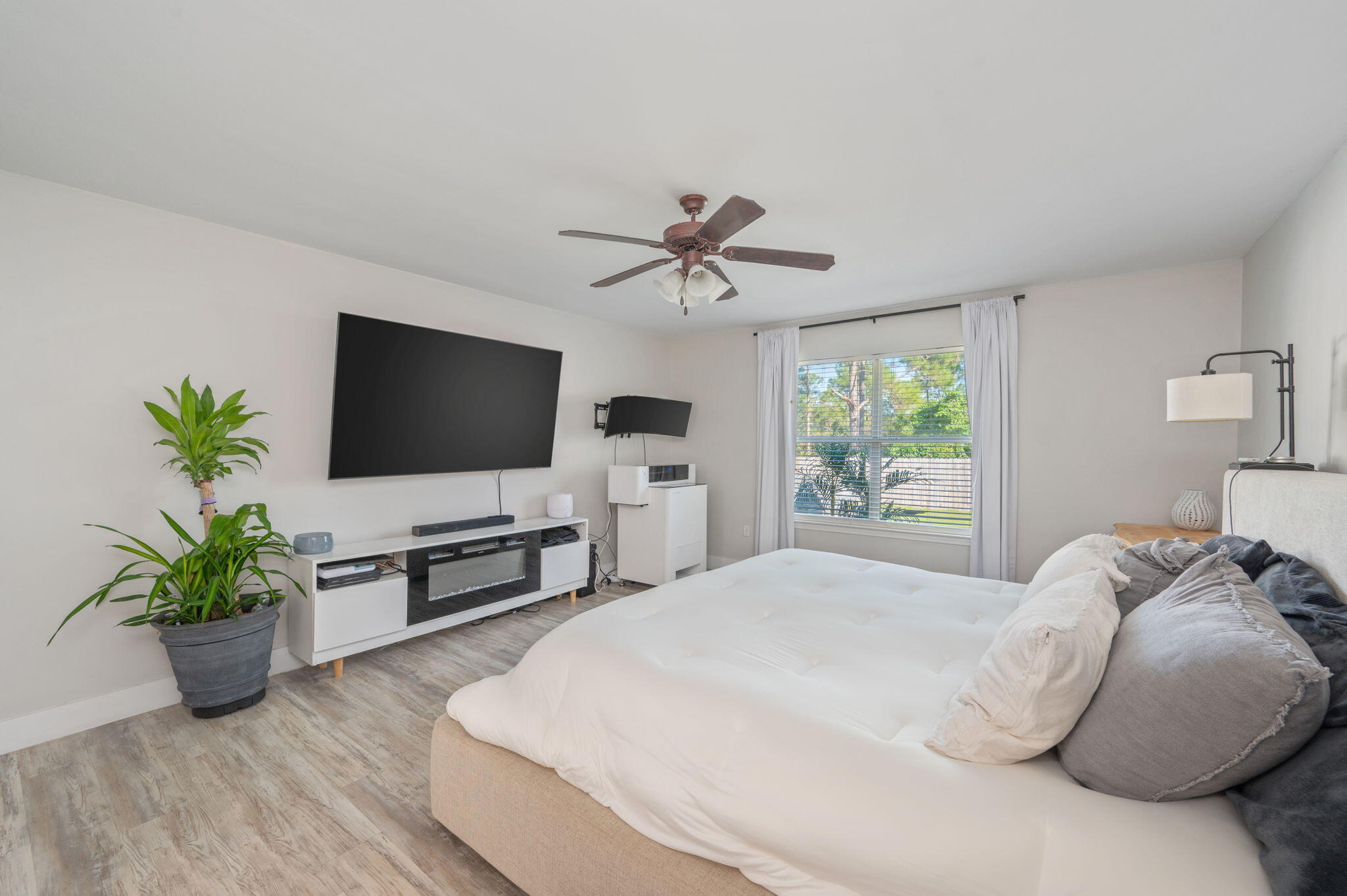 Bedroom with a large bed, ceiling fan, wall-mounted television, and curtained window.