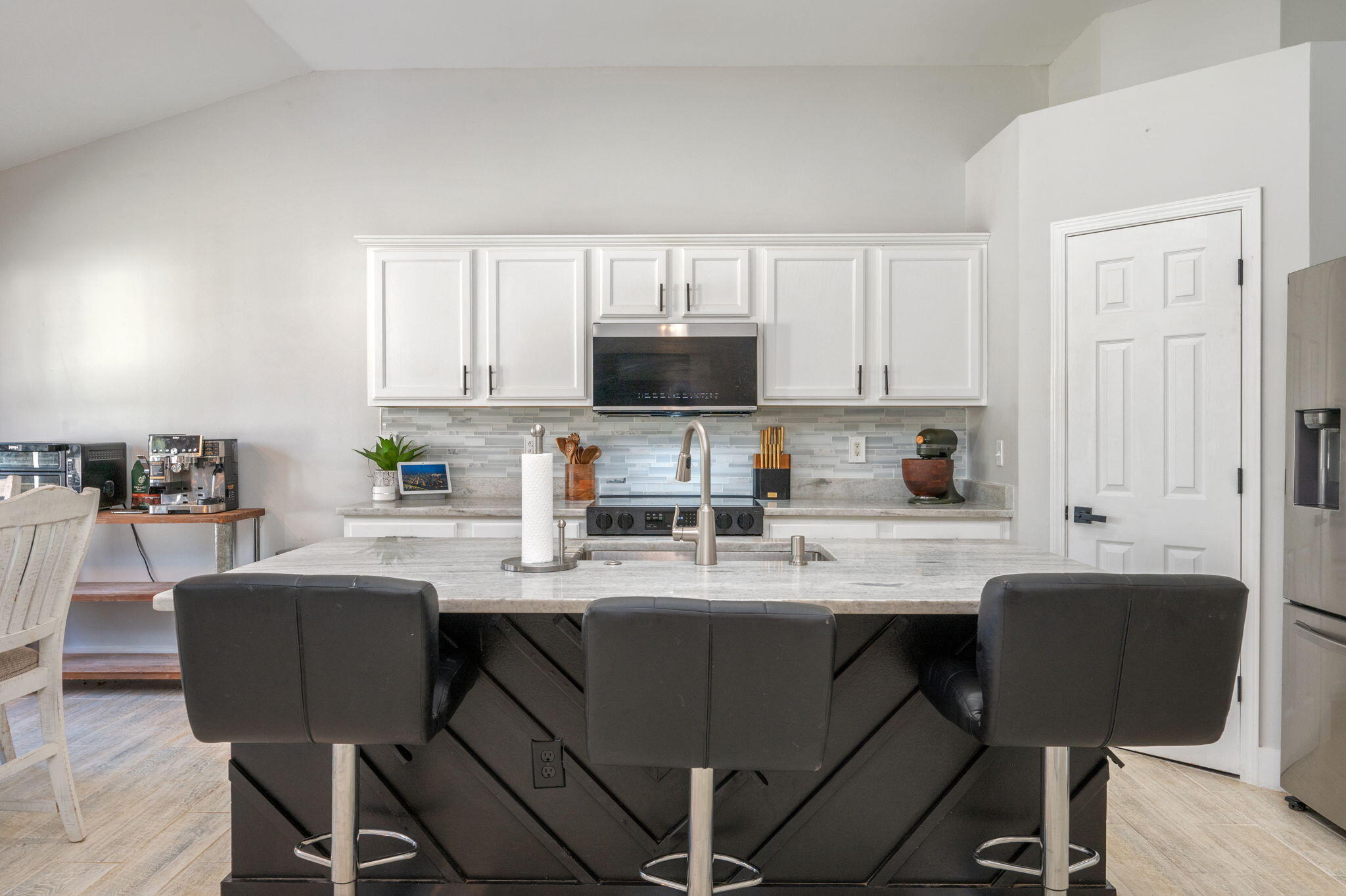 Kitchen with white cabinets and a large dark island topped with light stone and three bar stools.