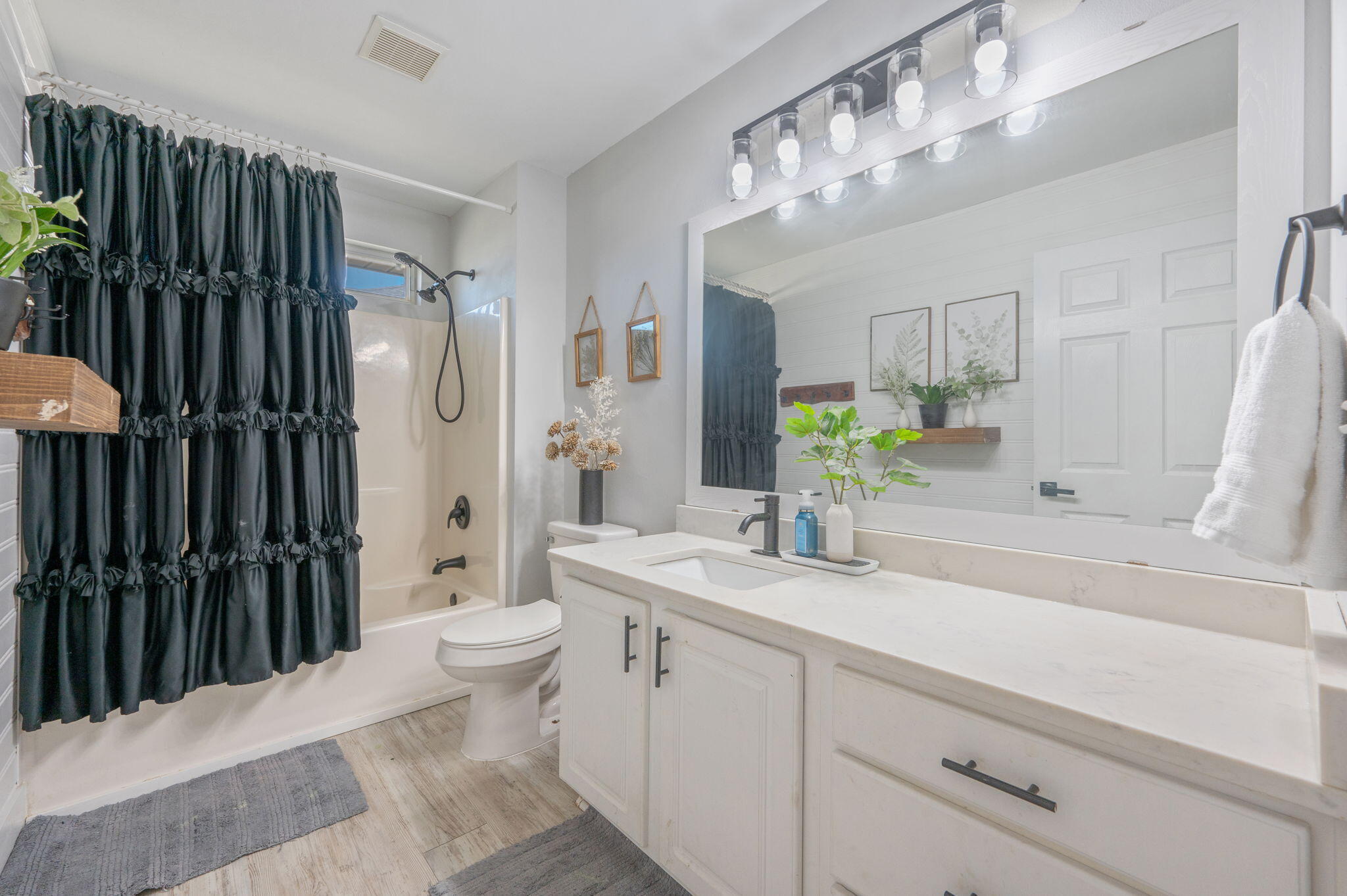 Bathroom with a white vanity and large mirror beside a tub with a black ruffled shower curtain.