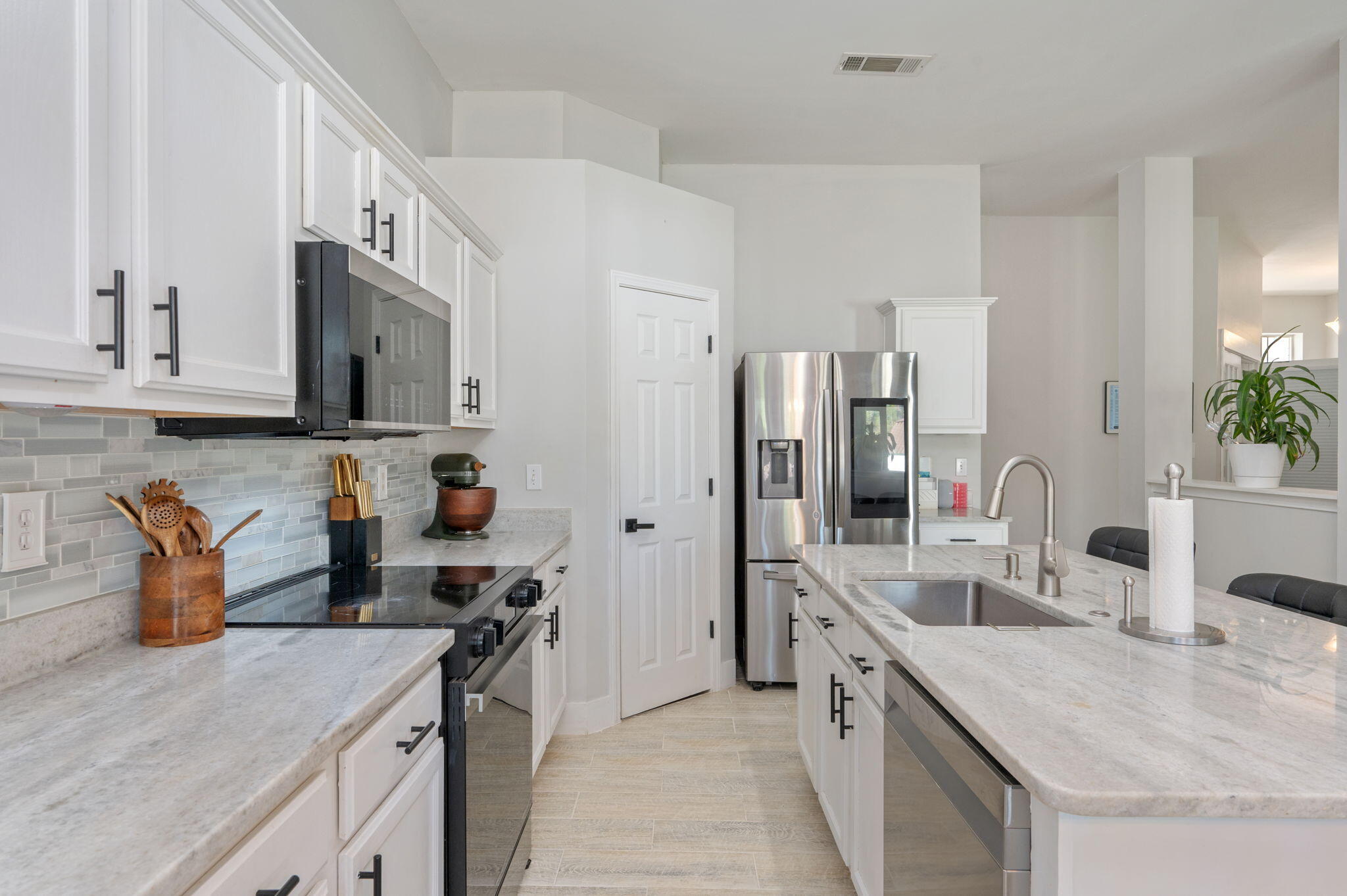 Kitchen with white cabinetry, gray tile backsplash, stainless steel appliances, and a large island sink.