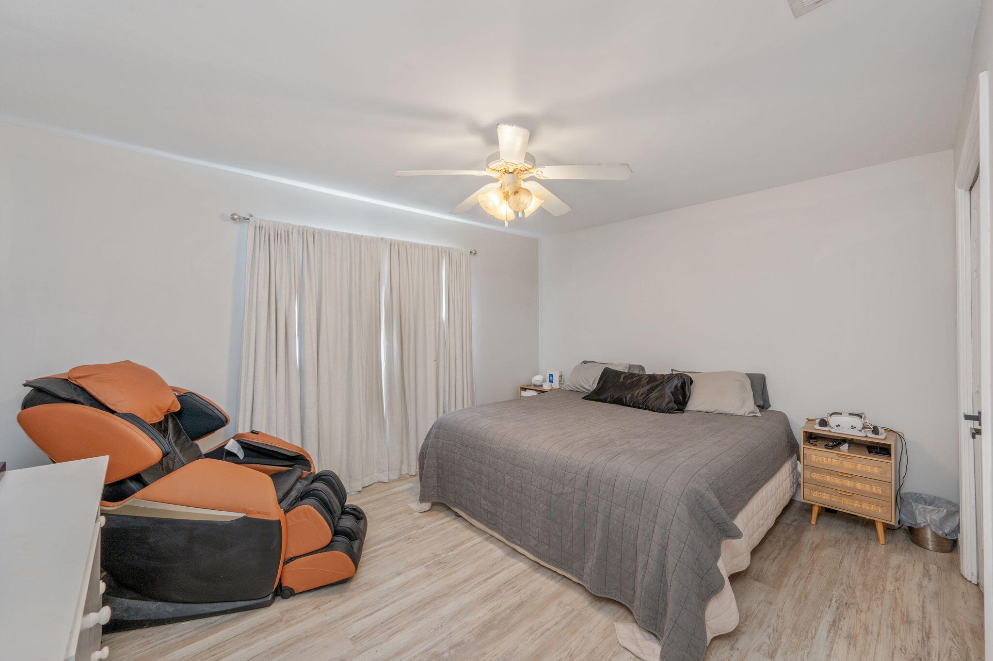 Bedroom with a gray-covered bed, ceiling fan, and orange-and-black massage chair.
