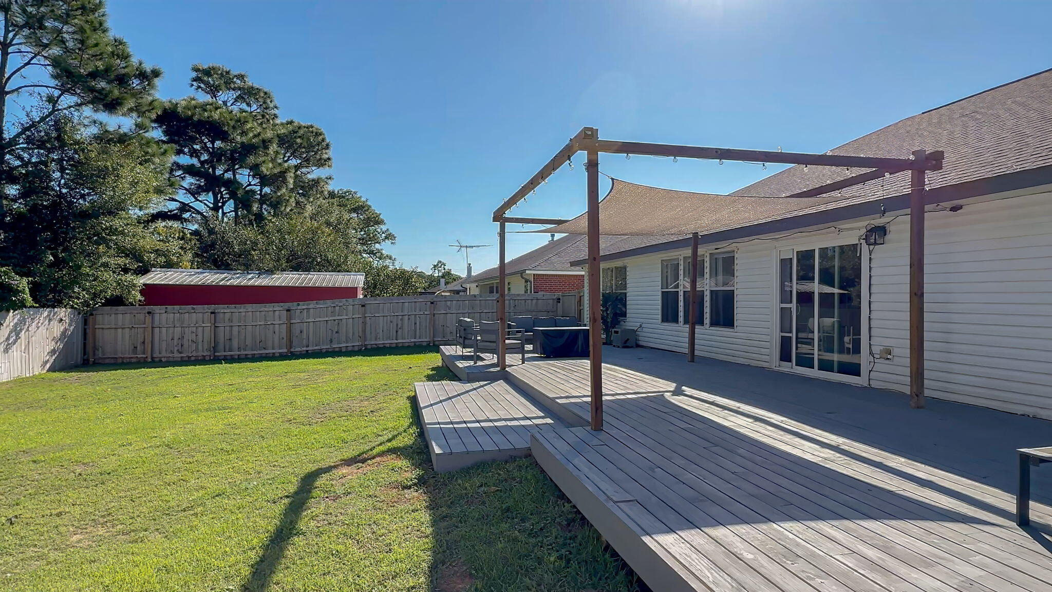 Backyard deck with a pergola, shade canopy, outdoor seating, and fenced lawn.
