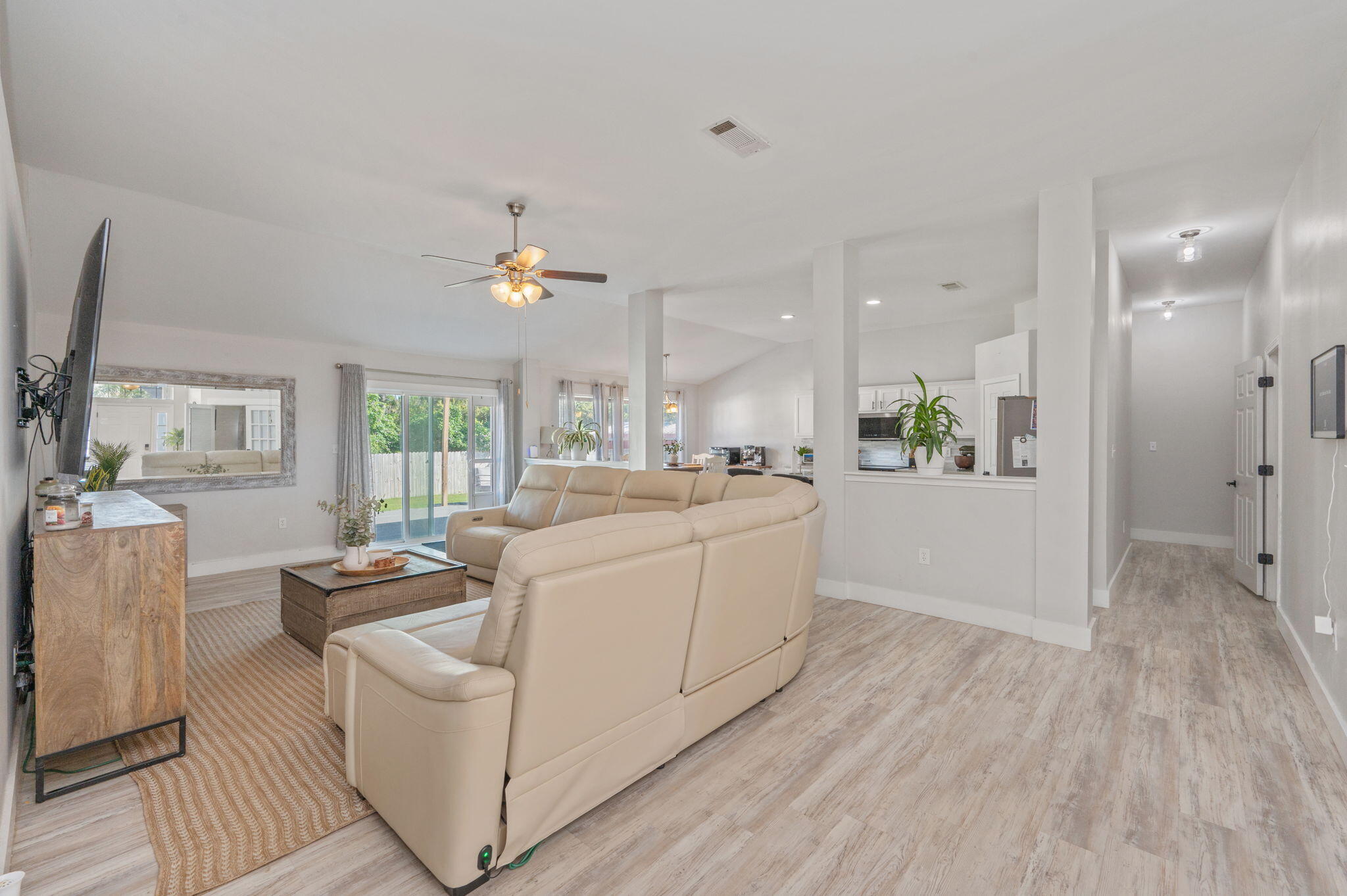 Open-plan living room with a cream sectional, sliding glass doors, and a view into the kitchen.