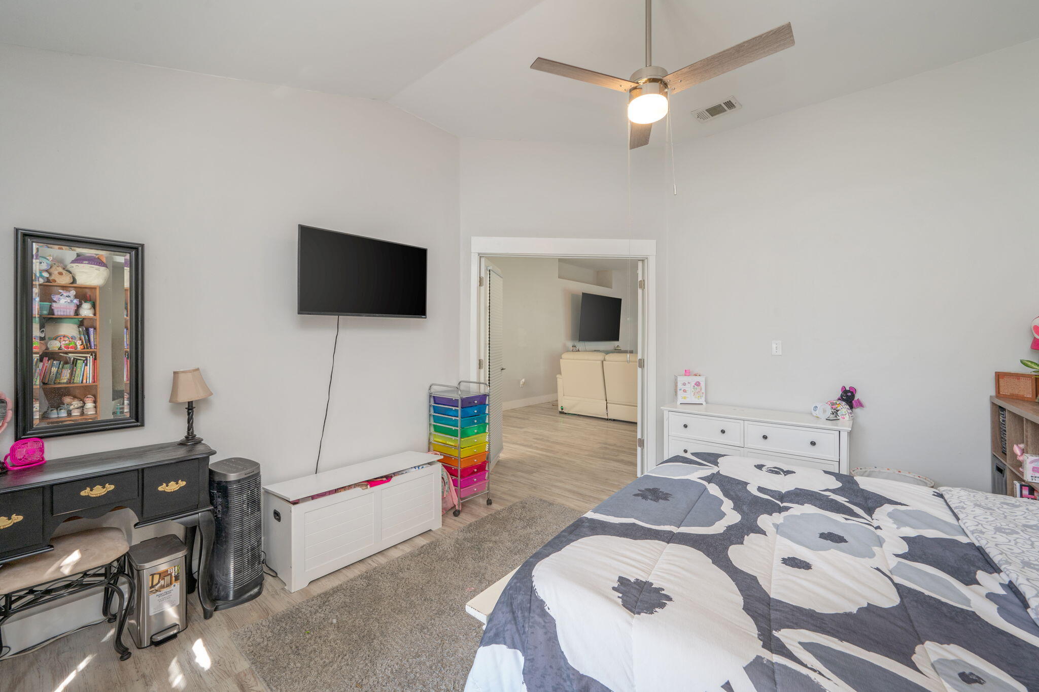 Bedroom with a gray-and-white patterned bedspread, ceiling fan, and open doorway to the living area.
