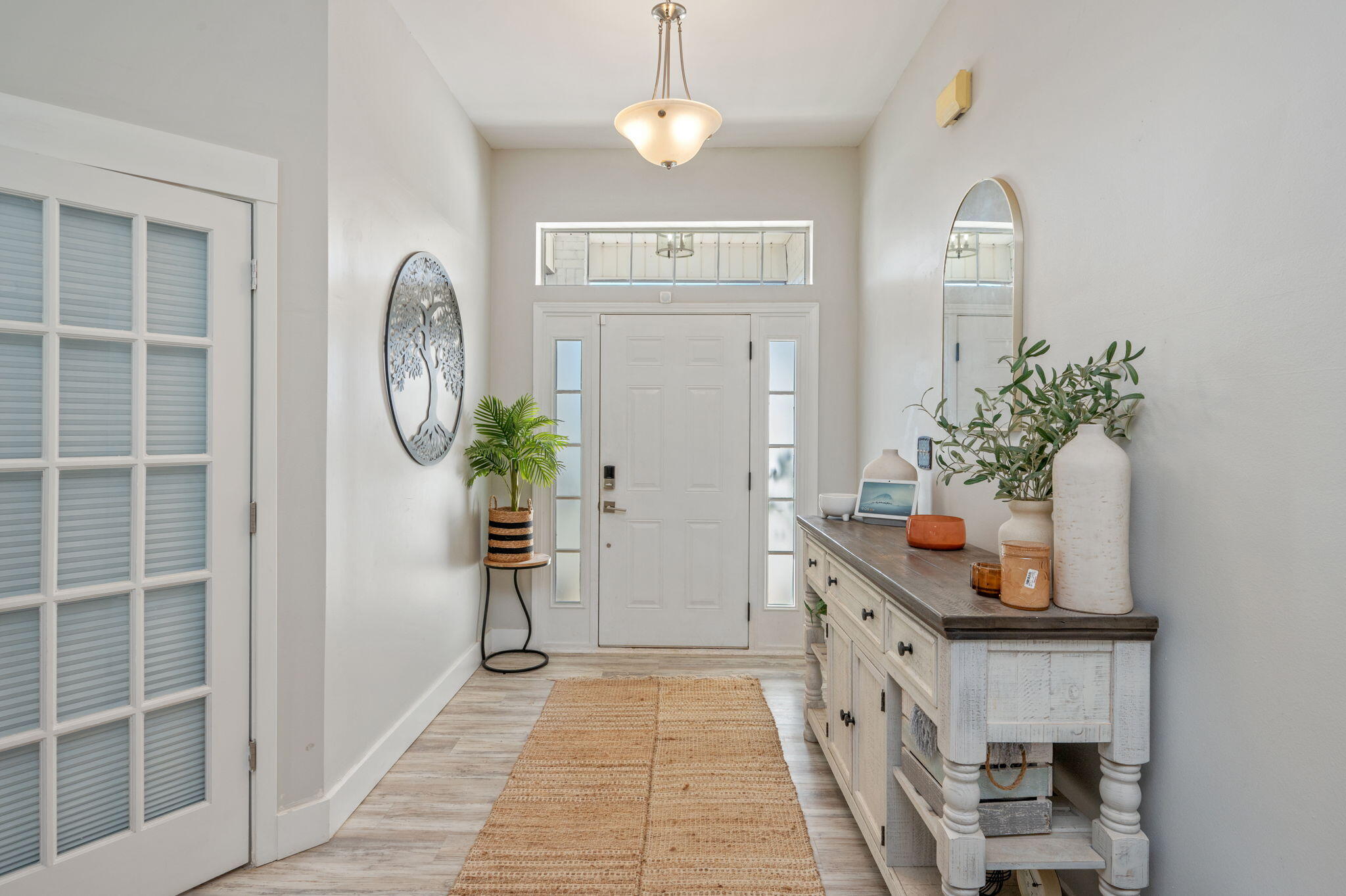 Bright entryway with a white front door, transom window, woven runner, and console table.