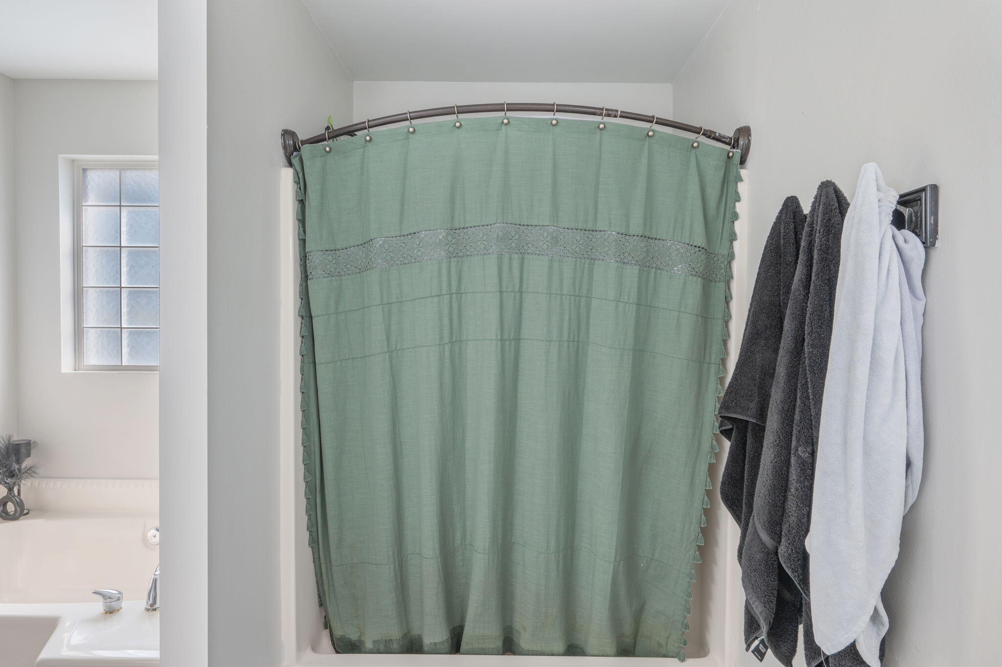 Bathroom with a green shower curtain, hanging towels, and part of a bathtub and window.