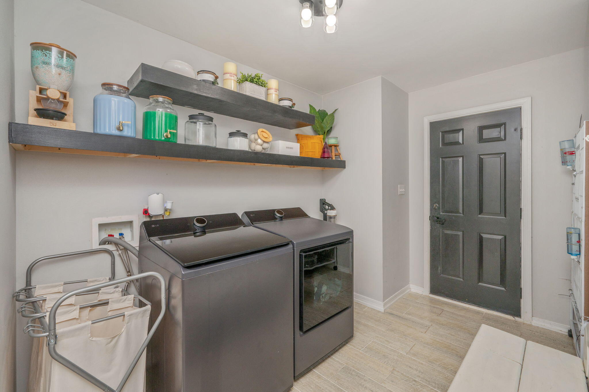 Laundry room with gray washer and dryer, floating shelves, and folding drying racks.