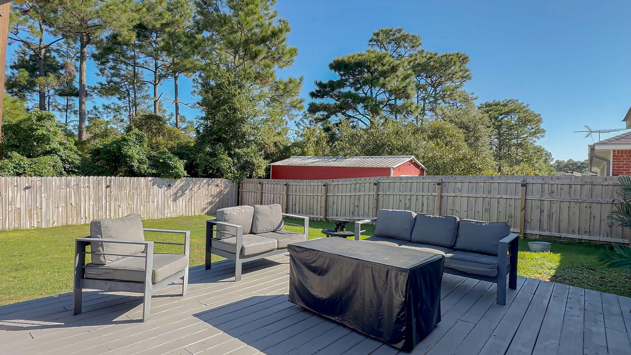 Backyard deck with outdoor lounge seating, a covered table, and a tall wooden privacy fence.