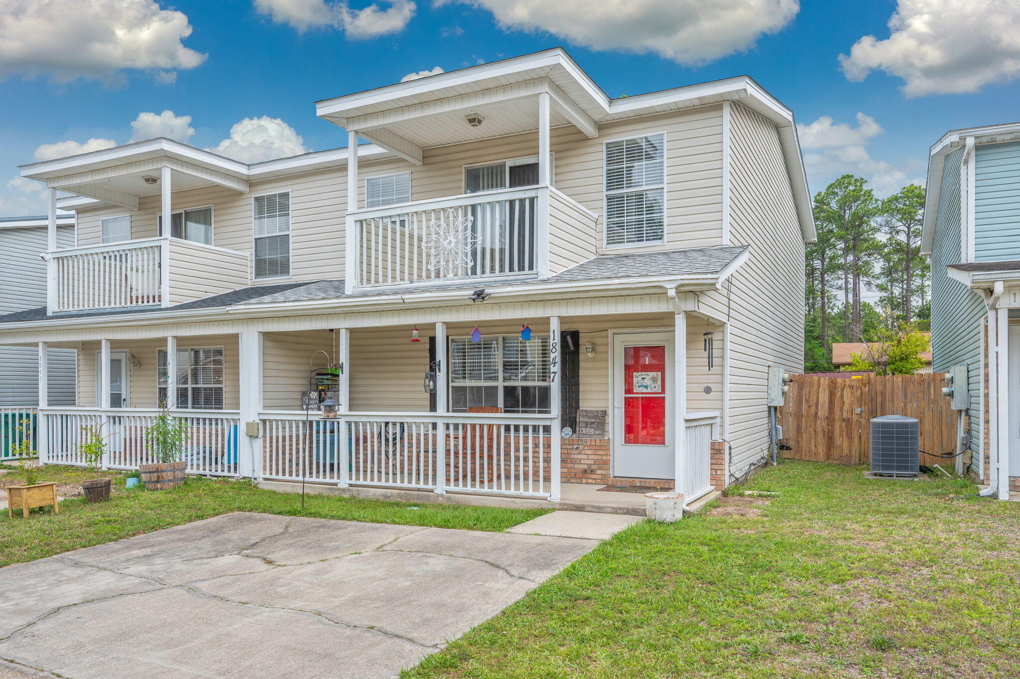Two-story beige home with white-railed porches, a red front door, and a concrete driveway.