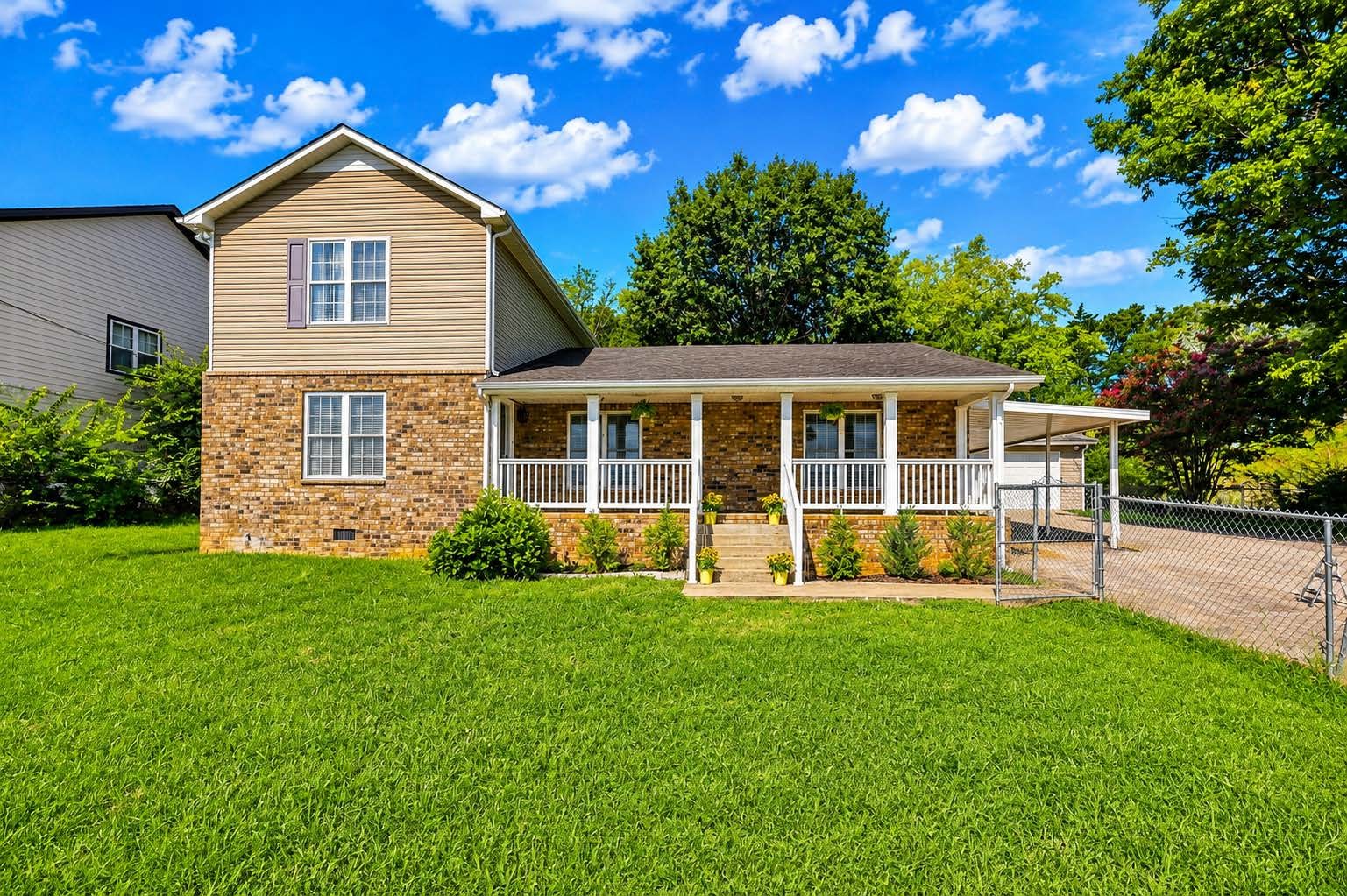 Two-story brick and siding home with a covered porch, broad lawn, and fenced driveway.