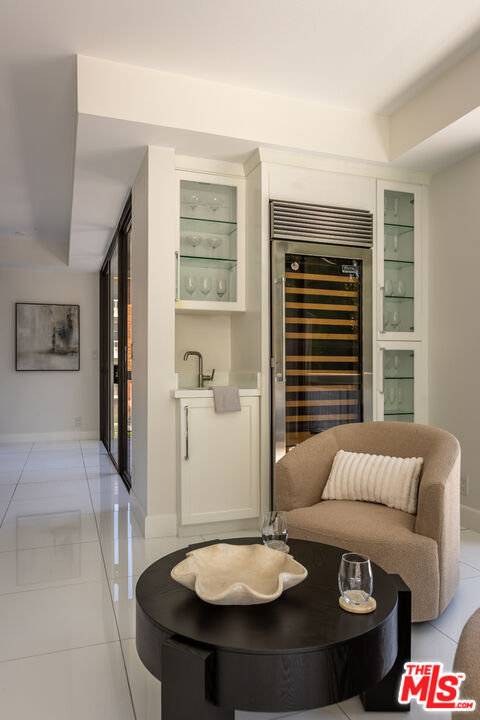 Condo living area with a built-in wine refrigerator, glass cabinets, and a curved armchair.