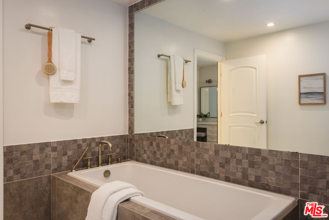 Bathroom with a built-in tub, brown tile surround, brass fixtures, and a large mirror.