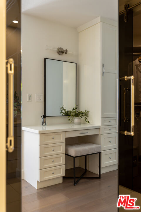 White built-in dressing vanity with drawers, tall cabinet, large mirror, and cushioned stool.