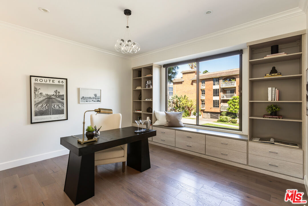 Staged home office with built-in shelving and a wide window overlooking a landscaped courtyard.