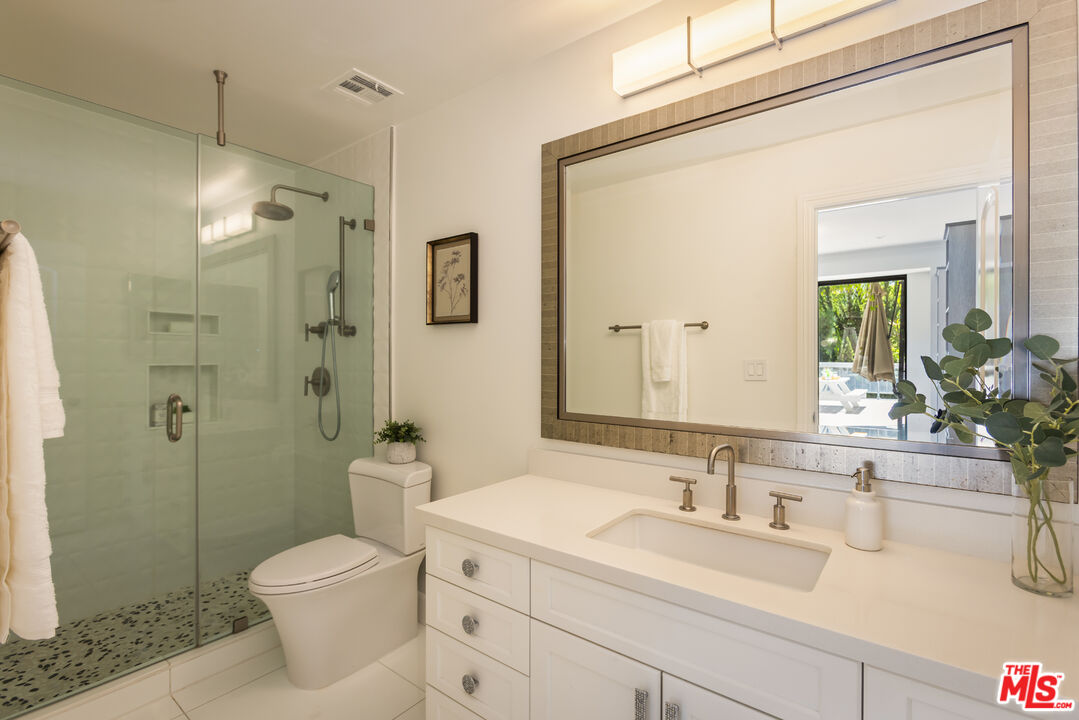 Bathroom with a glass-enclosed shower, white vanity, and large framed mirror.