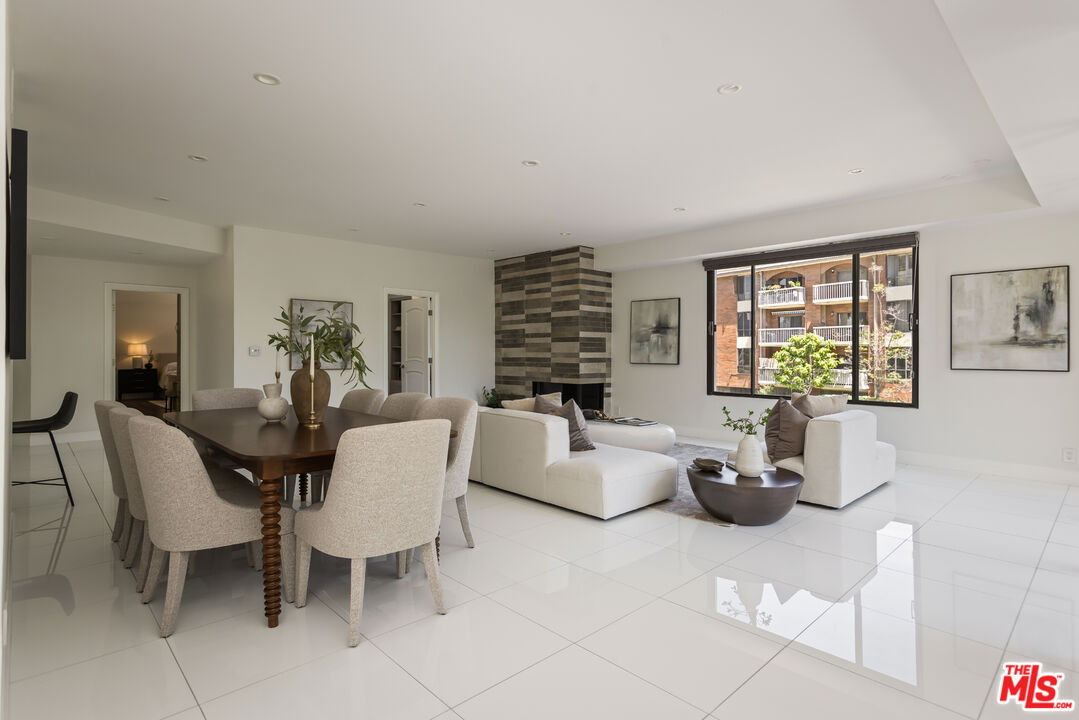 Open-plan living and dining room with white tile floors, white sofas, and a striped tile fireplace surround.