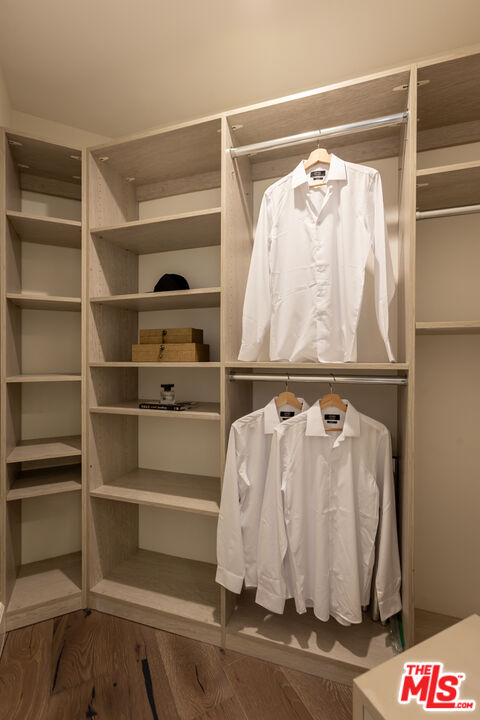 Walk-in closet with light wood built-ins, white shirts on hangers, and dark wood flooring.