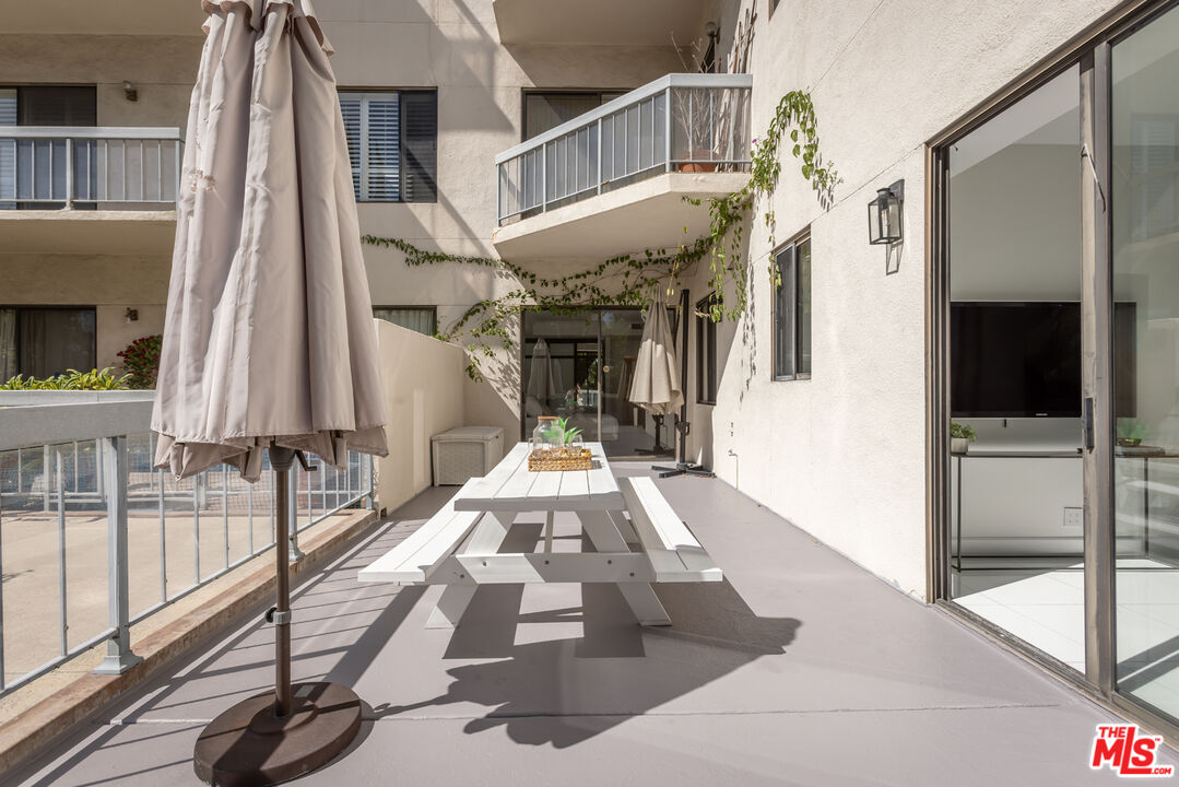 Apartment terrace with a white picnic table, closed umbrellas, and sliding glass doors.