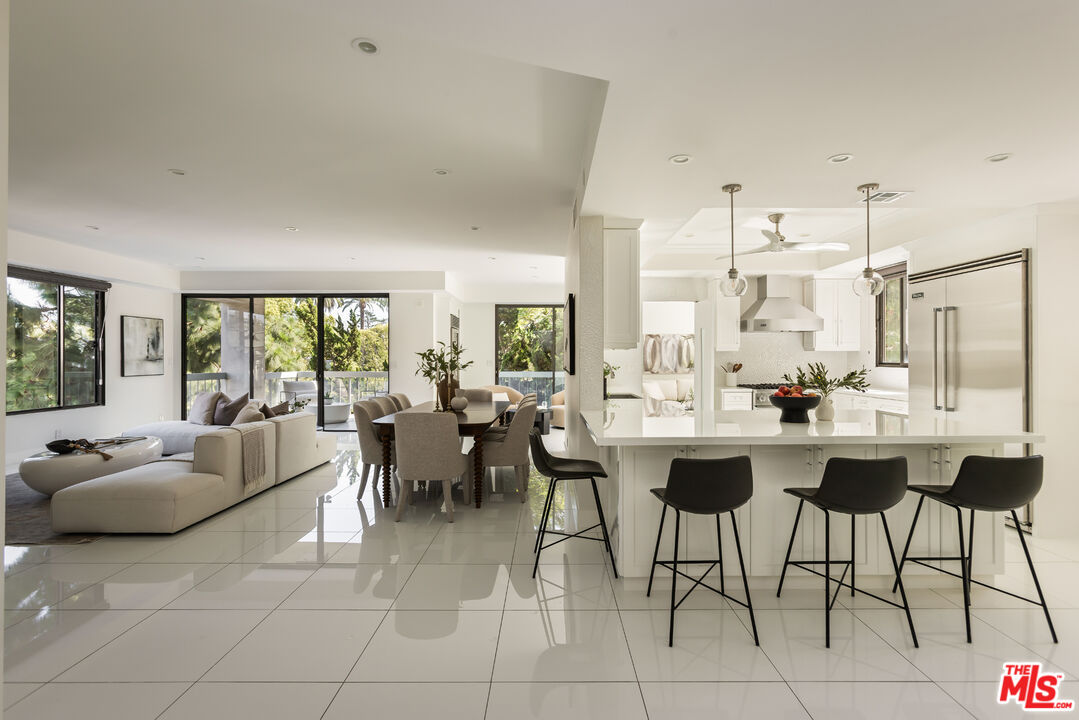 Open-plan living room, dining area, and white kitchen with an island and black bar stools.