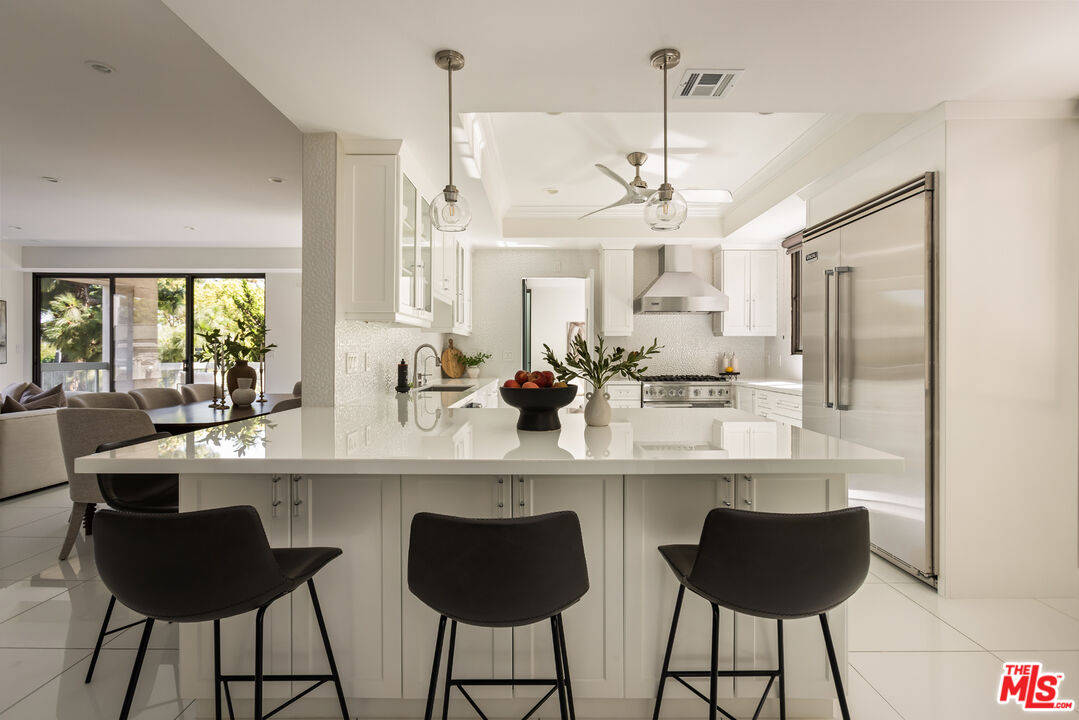 Modern white kitchen with a large island, dark bar stools, and stainless steel appliances.