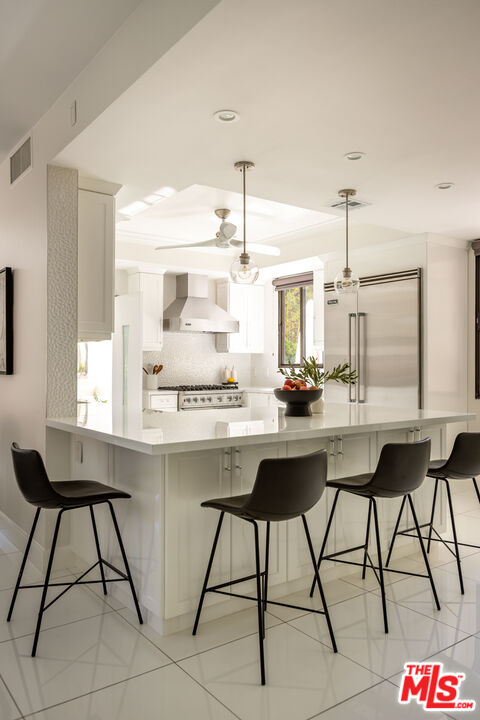 Bright white kitchen with a large island, dark bar stools, and stainless steel appliances.
