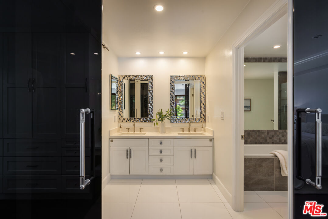 Bathroom with a white double vanity, patterned-framed mirrors, dark cabinetry, and an adjoining tiled bathtub.