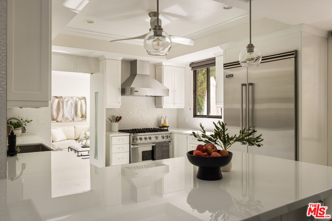 Bright white kitchen with a large island, stainless steel Viking appliances, and pendant lights.