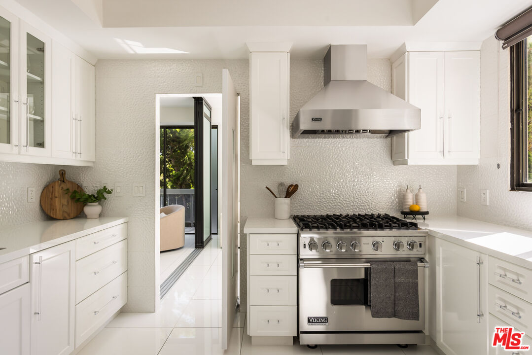 White kitchen with a stainless-steel Viking range and oversized range hood.