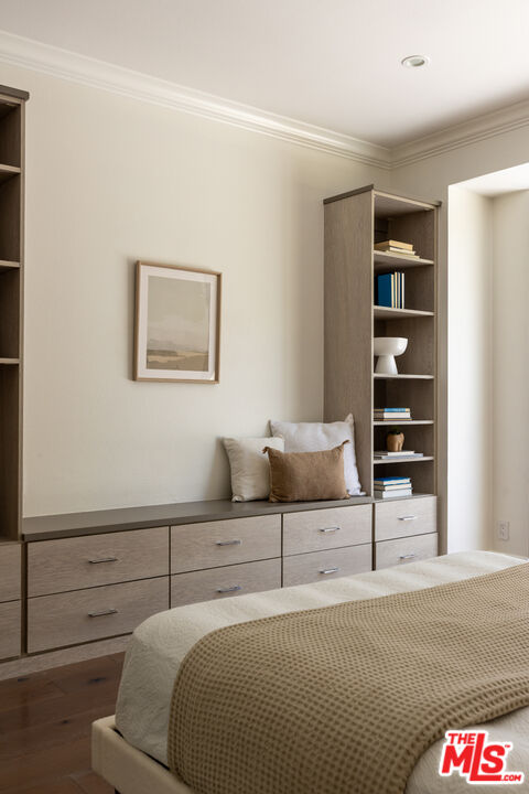 Bedroom with built-in taupe drawers and shelving, a neatly made bed, and framed wall art.