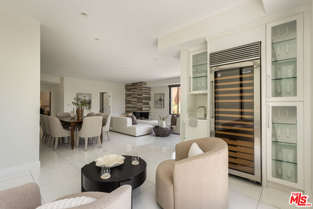 Open-plan living and dining room with cream seating, white tile floors, and a built-in wine refrigerator.