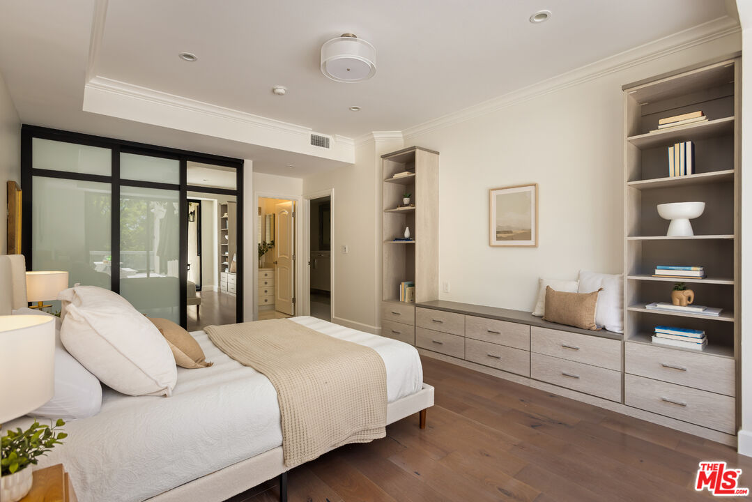 Staged bedroom with built-in shelving, a black-framed glass partition, and warm wood flooring.
