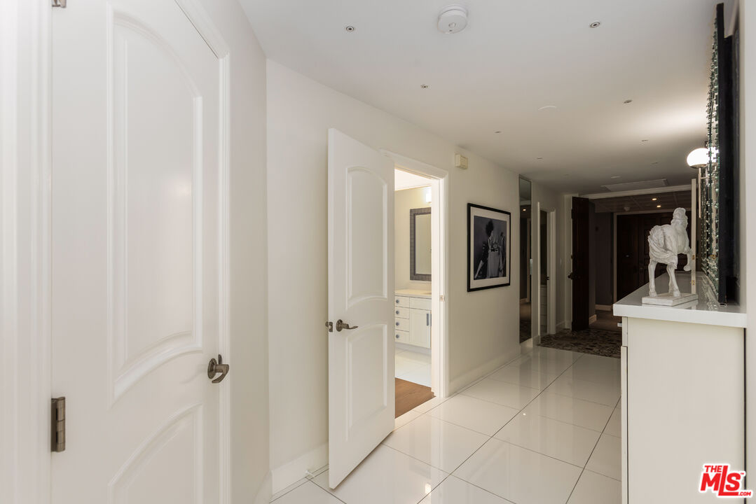 Condominium hallway with glossy white tile floors, paneled doors, and a sculpture on a console.