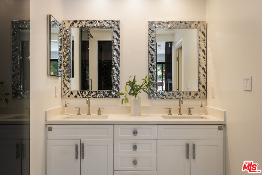Bathroom double vanity with white cabinetry, chrome fixtures, and ornate silver-framed mirrors.