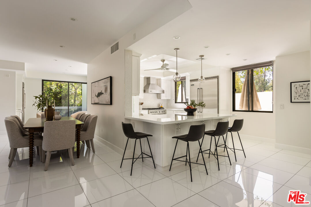 Open-plan kitchen and dining area with a white island, black stools, and large windows.