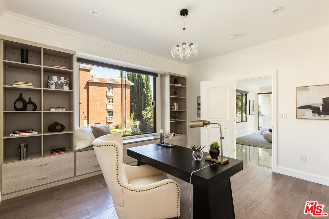 Furnished home office with built-in shelving, a black desk, and a large window overlooking trees.
