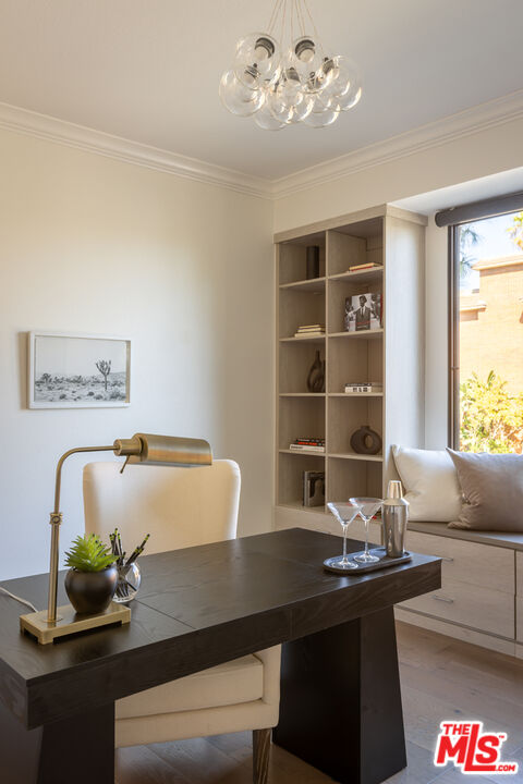 A staged home office with a dark desk, built-in shelving, and a cushioned window seat.