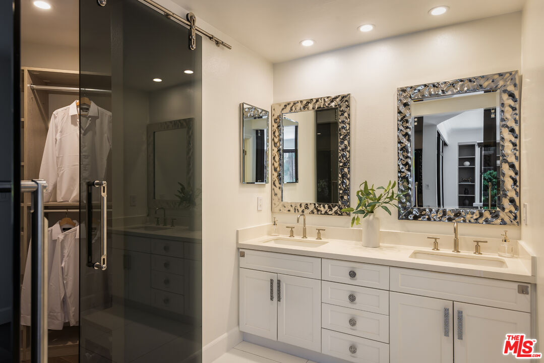 Bathroom with a white double vanity, ornate mirrors, and a dark glass shower enclosure.