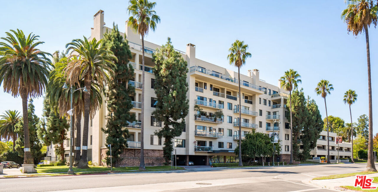 Multi-story residential building with balconies and palm trees along the street.