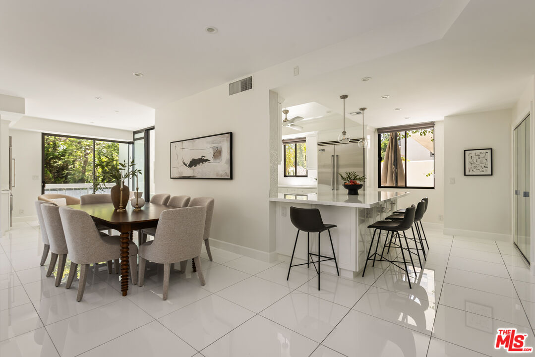 Open-plan dining room and kitchen with a wood dining table, white island, and glossy tile floors.