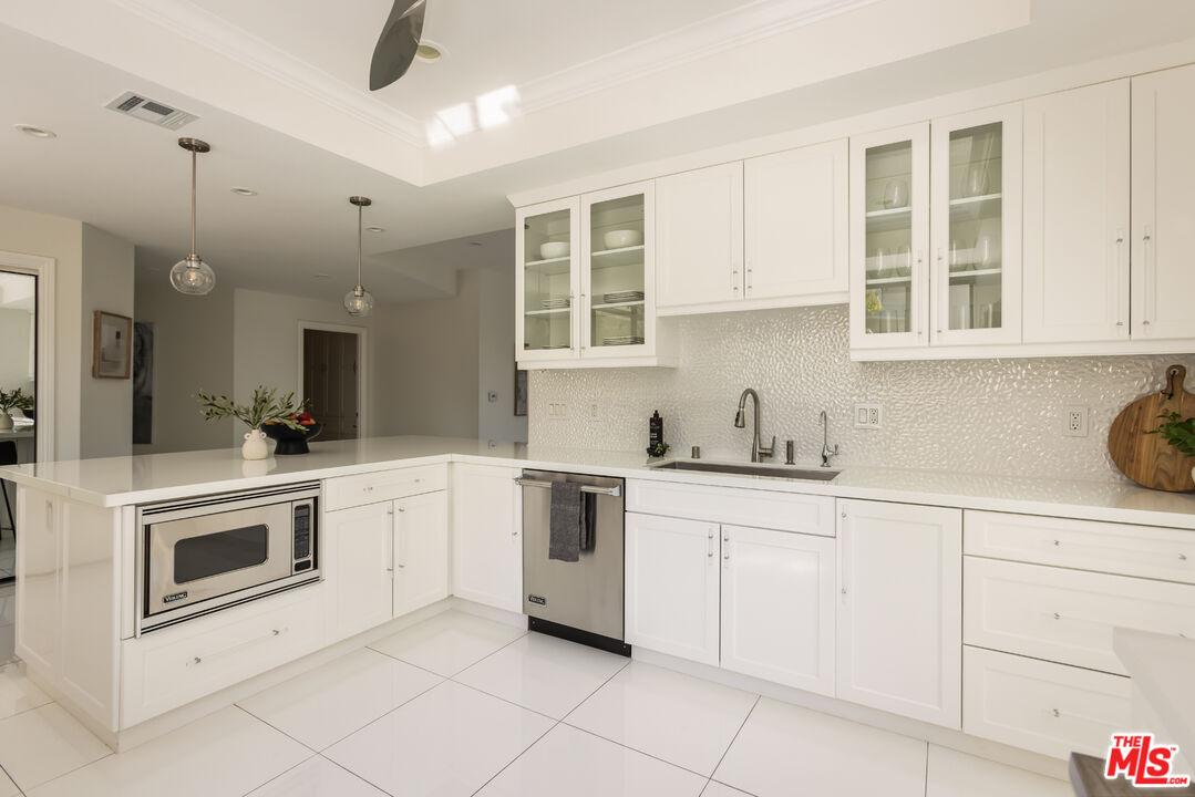 White kitchen with a broad peninsula, glass-front cabinets, and a textured backsplash.